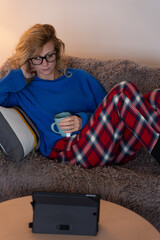 Woman relaxing on sofa watching tablet and drinking tea