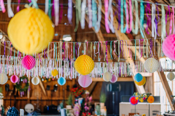 Bright ribbons and paper lanterns hang from the ceiling of a rustic wooden venue, creating a festive atmosphere for a celebration. Suitable for commercial use.