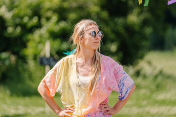 Woman in colorful hippie-style outfit and sunglasses standing confidently outdoors on a sunny day,...