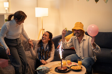 Friends celebrating birthday at home with cake and sparklers