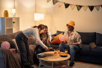 Friends celebrating birthday party at home with sparklers and cake