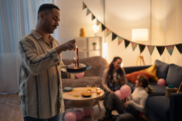 Man lighting candles on birthday cake at a party with friends