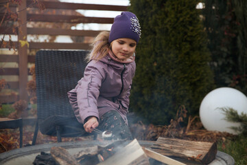 An eight-year-old girl roasts marshmallows on an autumn day near a country house.  Family leisure with kids at autumn.