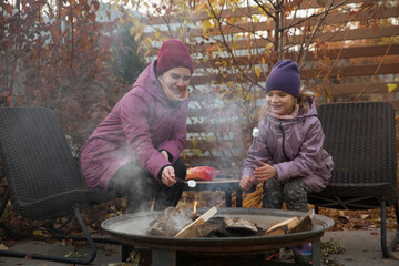 family mom and daughter is eight years oldl roasts marshmallows on an autumn day near a country house.  Family leisure with kids at autumn.
