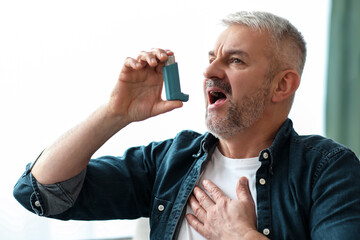 Senior man touching chest and using inhaler at home, suffering from asthma attack, closeup, copy...