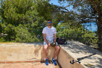 Man sitting outdoors in summer with sunglasses and hiking poles