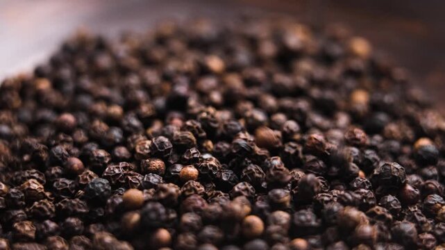 Dried peppercorns of black pepper falling in slow motion into a brown bowl