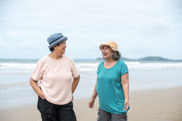 Senior women joyful talking and laughing while standing on beach. Asian mature female retired on...