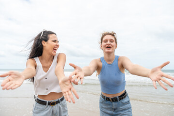 Two young women joyful arms raised and laughing together on the tropical beach. Female with friend...