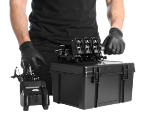 Close up view of a person in black gloves handling a black tool case and a small black device. The person is wearing dark clothing. Black is the dominant color