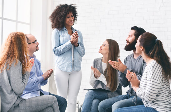 Young people clapping to black woman, supporting and cheering her up at rehab group meeting