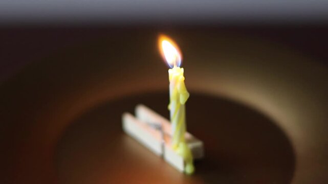 Una toma de cerca de una vela blanca con amarillo de cumplea&ntilde;os  con llama colocada en un gancho de madera en un fondo oscuro  