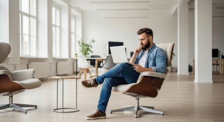 Young entrepreneur sitting in a modern chair, focused on his laptop in a bright office space