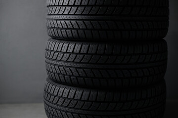 Three stacked black car tires with detailed tread pattern against a solid gray wall in a minimalistic indoor setting