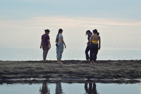 All four teenage girls are now standing freely again on the beach near the morning tide, preparing for another yoga session.