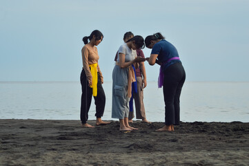 On the beach, two out of four teen girls gently join their hands in front of their chest to end...