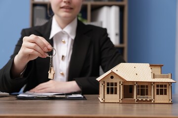 Real estate agent holding key and house model at desk in office, closeup