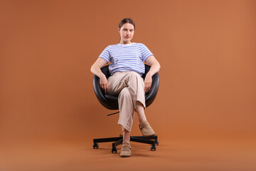 Beautiful young woman sitting on armchair against brown background