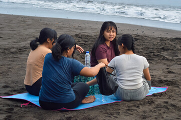 With the food almost finished, the girls continue chatting in comfort, enjoying the remaining moments of their peaceful beach morning picnic together.