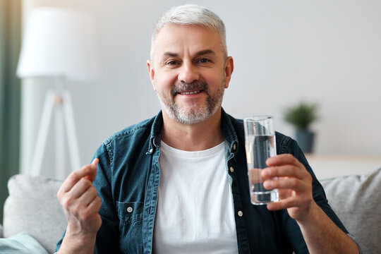 Treatment, medicine, medication, pills, vitamins, supplements concept. Smiling senior man with glass of water taking pill. Closeup of mature grey-haired man with medicine, copy space