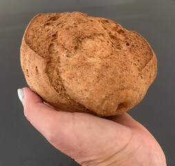 Closeup image of a woman holding a small loaf of wholemeal bread in her hand against a grey background