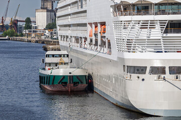 A small tugboat assisting a large cruise ship as it enters the port. Harbor tug helping guide the vessel to dock. Maritime transportation and port operations