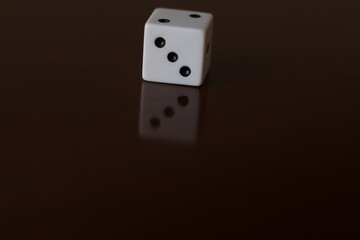 Una toma de cerca  de uno o varios dados blancos para juego en una mesa de color marrón oscuro...