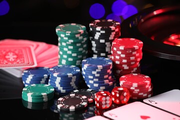 Casino chips, playing cards and dice on mirror surface against blurred lights, closeup