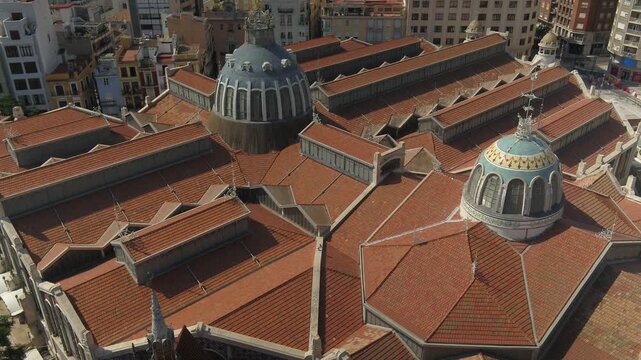 Toma a&eacute;rea descendente con dron sobre el tejado del Mercado Central de Valencia, con c&aacute;mara en contrapicado revelando los edificios de la ciudad