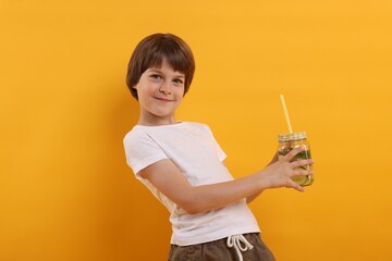 Cute little boy with mason jar of lemonade on orange background. Refreshing drink