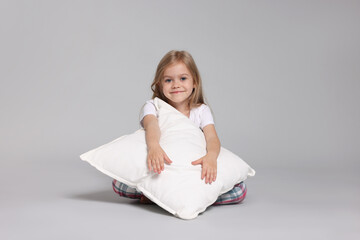 Cute little girl in pajamas with pillow on grey background