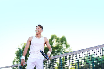 Young man playing tennis at court on sunny day, low angle view. Space for text