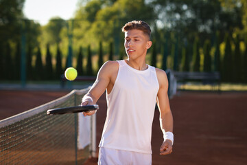 Young man playing tennis at court on sunny day