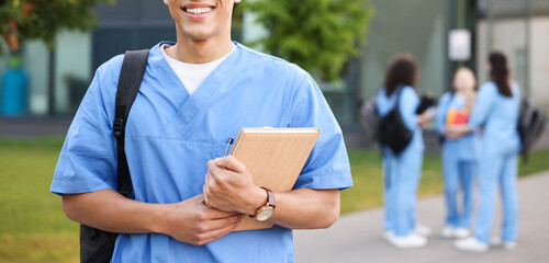 Medical student in uniform with backpack and notebook outdoors, selective focus