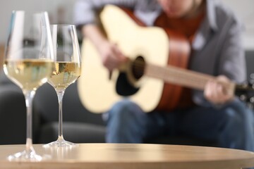 Glasses with white wine on table and man playing guitar indoors, selective focus