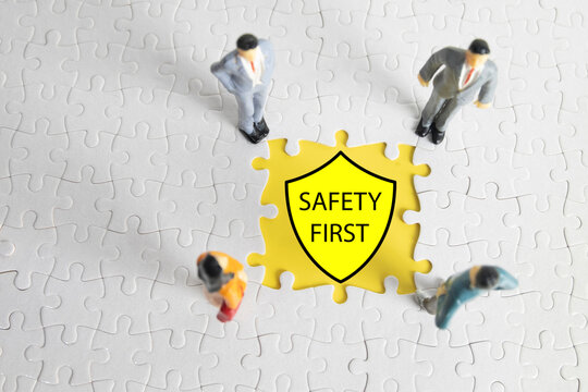 A team of miniature figures around a puzzle piece with a safety shield. For Occupational Health and Safety (OHS, HSE) and risk management.,Safety First concept for the workplace.