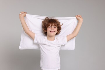 Cute little boy in pajamas with pillow on grey background