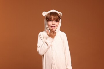 Cute little boy in pajamas on brown background