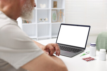 Senior man having online consultation with doctor via laptop at table indoors, closeup