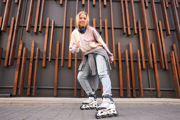 Beautiful young woman with roller skates near building outdoors, low angle view