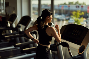 Woman Running on Treadmill in Modern Gym Next to Bright Windows