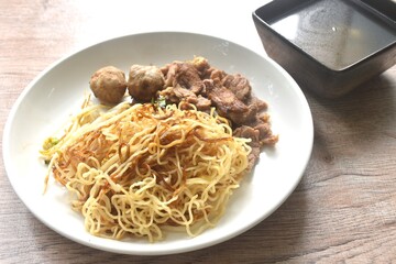 dry boiled Chinese yellow egg noodles with braised beef and meatball dressing black sweet soy sauce on plate with soup