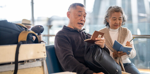 Senior asian couple sitting with luggage checking passport planning trip showing travel preparation...