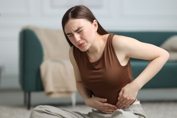 Woman suffering from abdominal pain on floor at home, space for text