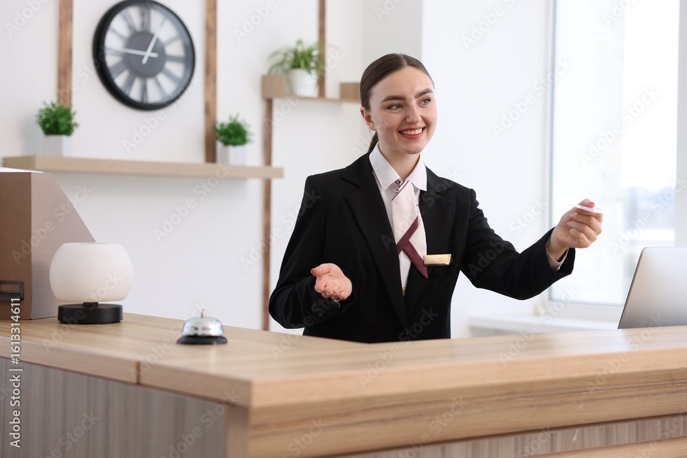 Poster smiling receptionist in uniform giving card key at reception desk in hotel