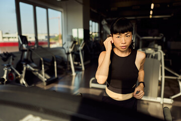 Fototapeta premium Focused Woman Running on a Treadmill in a Modern Fitness Gym