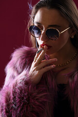 Beautiful woman in fur coat smoking cigarette on dark pink background, closeup