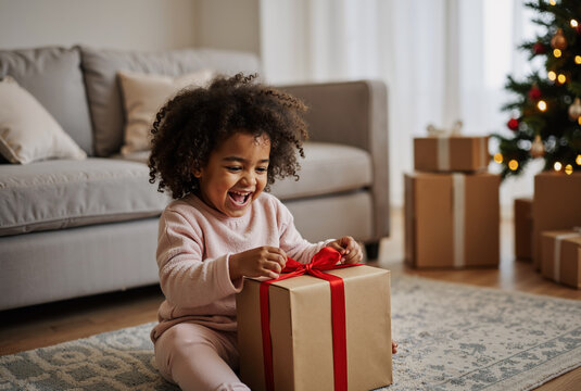 joyful young child with curly hair excitedly opening gift box near christmas tree in cozy living room celebrating holiday season with joy and anticipation
