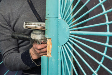 Closeup photo of man cutting old steel metal with angle grinder. Close-up of worker cutting lock on turquoise door with power tool