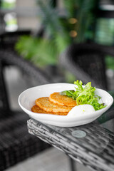 Top view of crispy potato pancakes with sour cream and green sauce, served on a white plate with...
